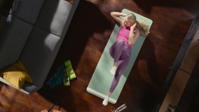 顶视图运动: 漂亮的女孩躺在家里的运动垫上做腹肌肘到膝仰卧起坐。健康，真正美丽的年轻女子在她的公寓里