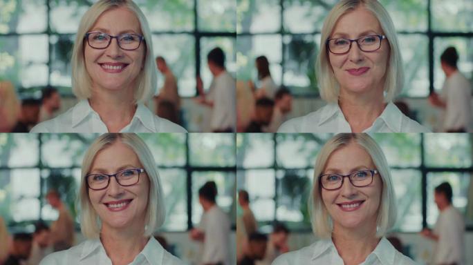 快乐的白人高级女商人，在办公室工作场所慢动作时对着镜头微笑的眼镜扬声器教练。