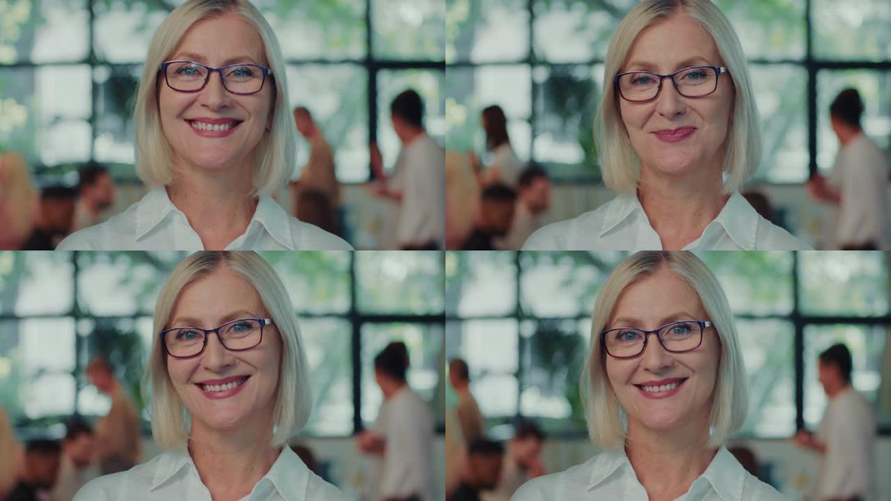 快乐的白人高级女商人，在办公室工作场所慢动作时对着镜头微笑的眼镜扬声器教练。