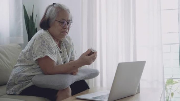 亚洲妇女拿着药瓶，在客厅的笔记本电脑上聊天。
