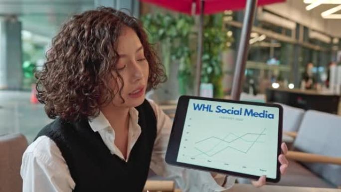 亚洲女性从事商业发展工作，展示数字平板电脑上的信息图表。