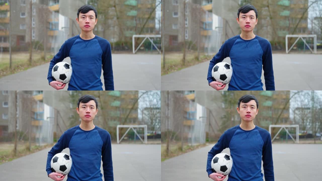 年轻的中国男子在城市运动场上拿着足球