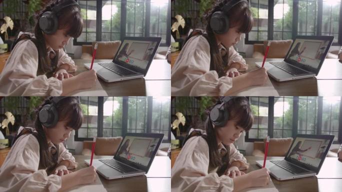 一个亚洲女孩正坐在家里专心地在线学习，并与哥哥在一起，通过平板电脑记下她所学到的知识。由于Covid