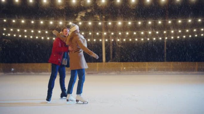 浪漫的冬夜: 滑冰夫妇在溜冰场上玩得开心。美丽的雪落在双人滑冰男孩和恋爱中的女友上，跳舞，牵手，拥抱