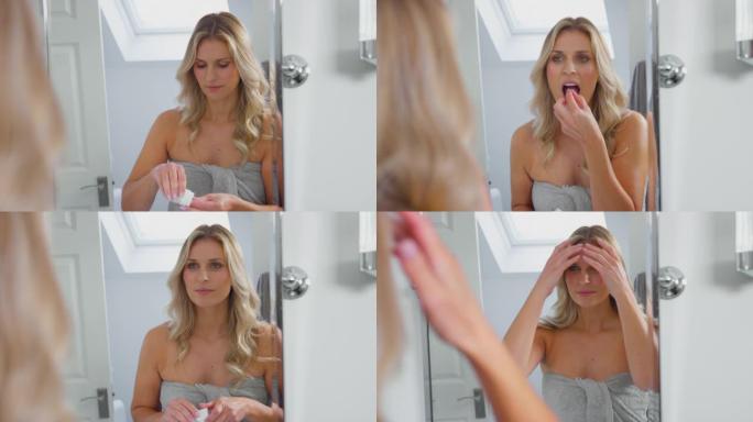成熟的女人在家里的浴室里照镜子，服用维生素片剂