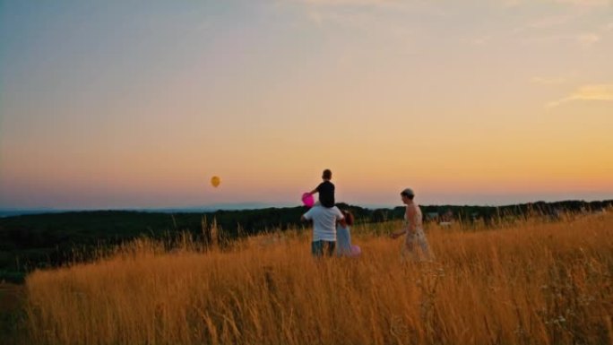 SLO MO家族在日落时分在草地中央向空中释放气球