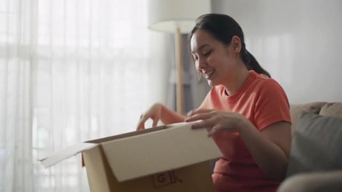 年轻亚洲女性消费者打开纸板箱获得邮政包裹