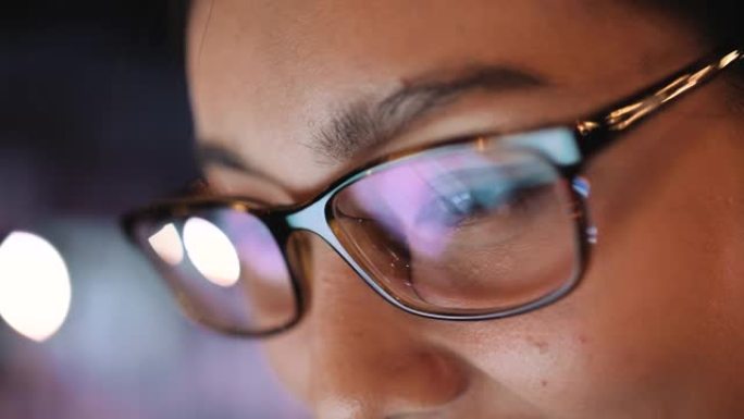 戴着眼镜的女人的眼睛在黑暗中盯着工作的平板电脑屏幕。