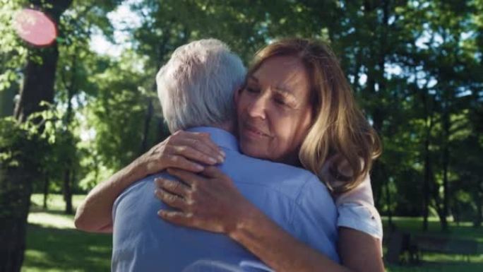 快乐微笑的成熟妻子的电影镜头正在给她的丈夫以情感的拥抱，作为绿色公园永远永恒的爱的标志。生活观念，家