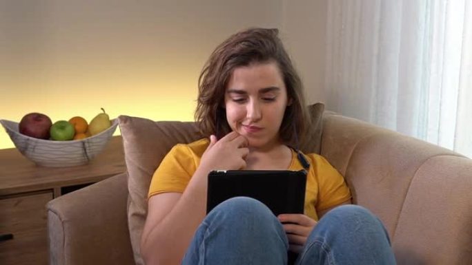 可爱的少女在沙发上看着平板电脑时喝着咖啡的视频。4k分辨率。