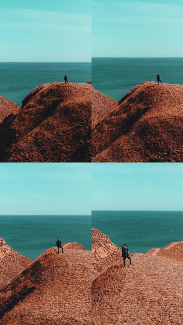 那个背着背包的男人站在山顶上，靠着海景