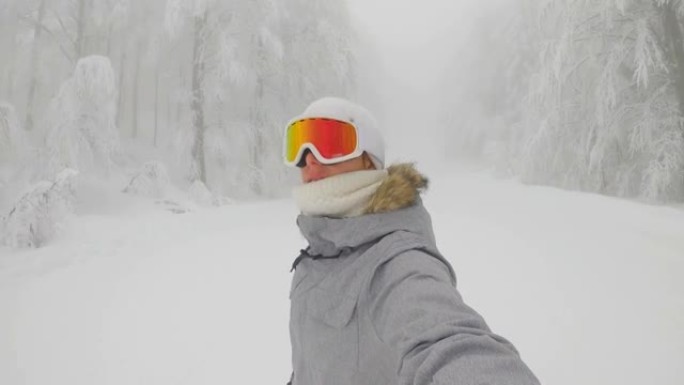 自拍照: 戴着橙色护目镜的女性滑雪者沿着滑雪胜地的斜坡骑行。