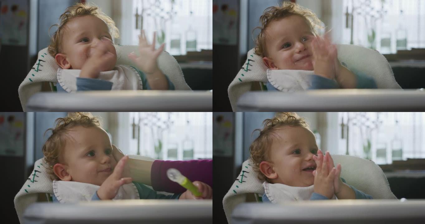 快乐的微笑的蹒跚学步的男孩的电影真实镜头坐在高脚椅上等待母亲准备饭菜时鼓掌。断奶、幸福、爱情、童年、