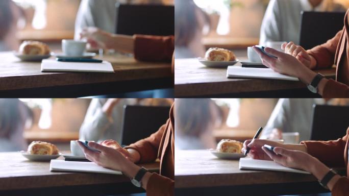 手，咖啡和电话与一名女商人在咖啡馆里写笔记，以自由职业者的身份进行远程工作。移动、社交媒体和咖啡店，