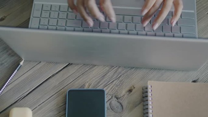 办公桌的俯视图，带有商务物品和笔记本电脑，女性双手在办公室打字
