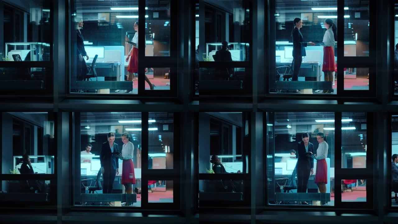外面的镜头: 两名女商人在办公室见面并握手。经理们站在窗边，看着一台平板电脑。员工谈论财务和业务发展