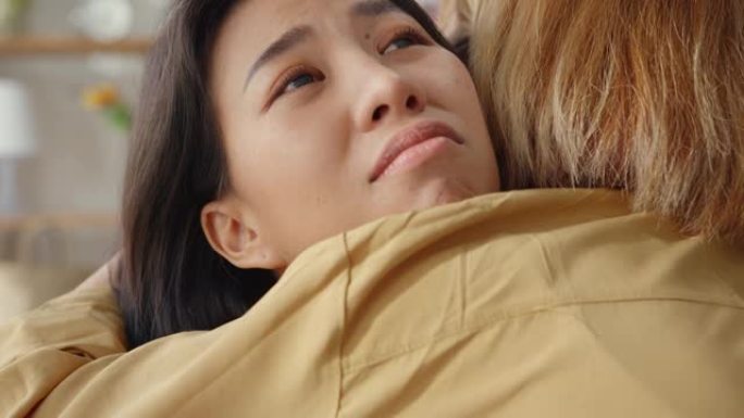 悲伤的年轻亚洲女人拥抱拥抱在家里的客厅和最好的朋友在艰难的时候互相支持，感到恶心和难过。
