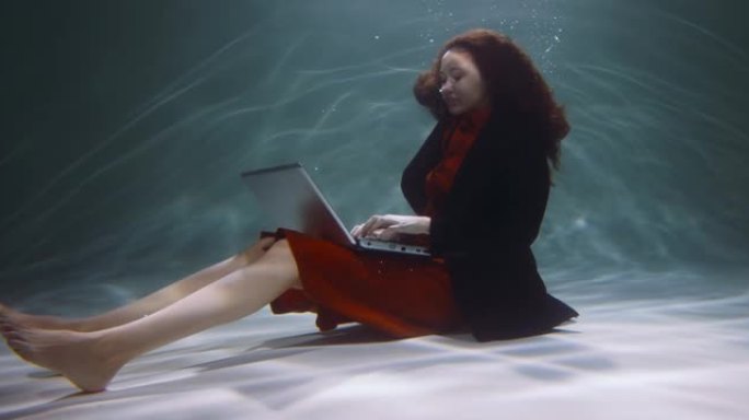 摆脱问题。年轻快乐冷静的自由职业者女商人用笔记本电脑在水下慢动作下工作。