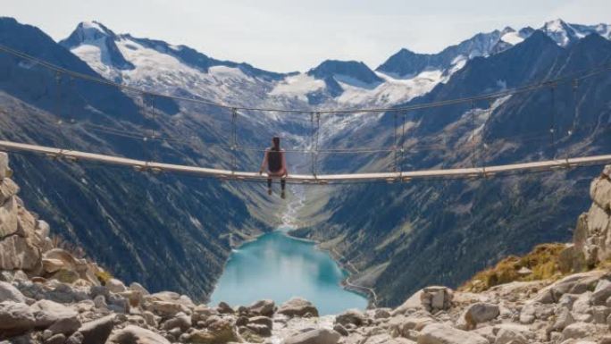 年轻的女徒步旅行者从山溪上的悬吊桥上欣赏壮丽的山谷湖景色