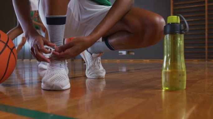 非裔美国女子篮球运动员在背景中与队友系鞋带