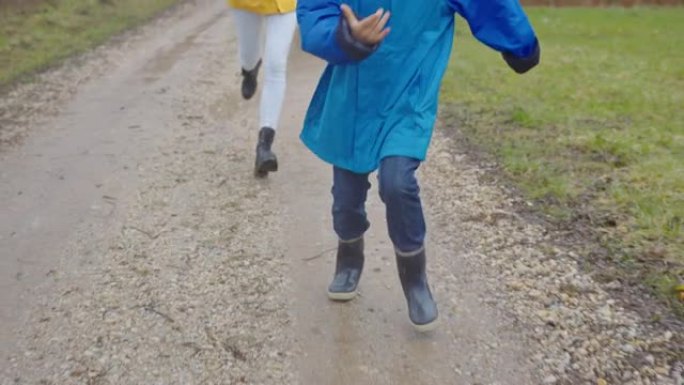 快乐的少女与兄弟在雨天在水坑中奔跑