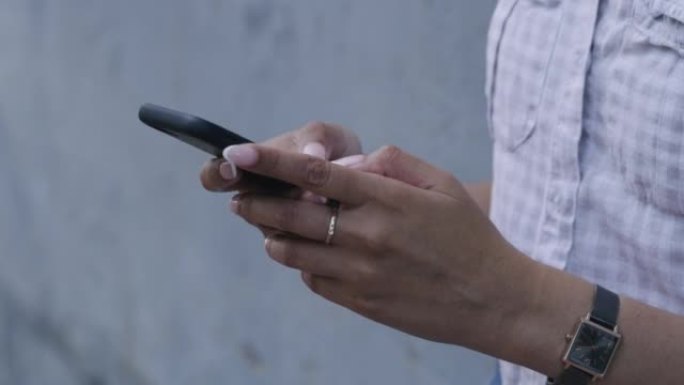 手机发短信和输入社交媒体帖子的特写镜头。女人独自一人站着，拿着，用技术联网，浏览互联网和连接。在城市