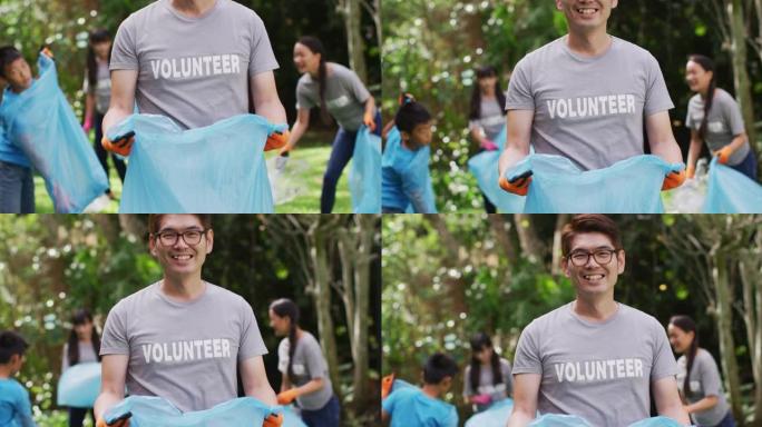 微笑的亚洲男子穿着志愿者t恤，拿着垃圾袋收集塑料垃圾