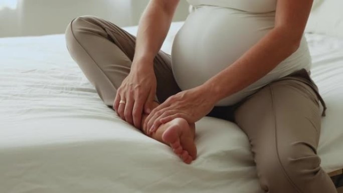 无法识别的孕妇坐在床上按摩她肿胀的脚踝