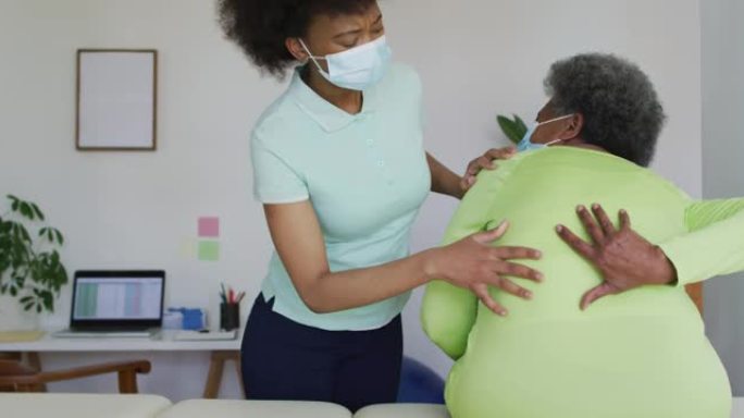 非裔美国女理疗师戴口罩协助资深女病人运动