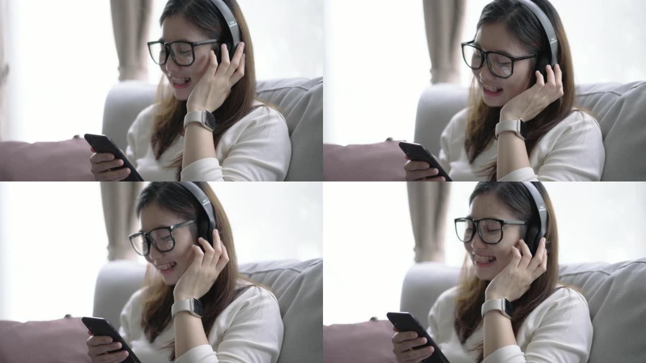 年轻的亚洲女性在客厅放松，用智能数字设备上的耳机听音乐