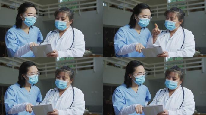 亚洲女医生戴口罩，使用平板电脑并在医院讨论的肖像