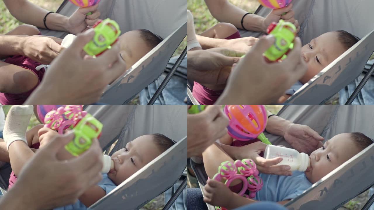 SLO MO的父母正在用奶瓶母乳喂养，并在公园里玩玩具拨浪鼓