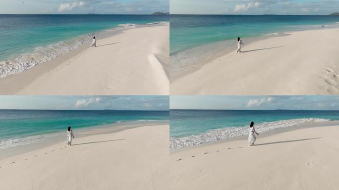 一名妇女在热带岛屿上的碧绿海水中沿着原始海滩的水边行走的空中后视