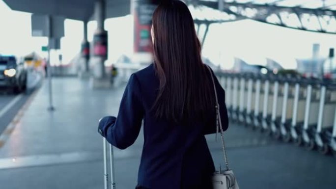 专横的女人走路，拉着行李箱在机场入口处寻找司机
