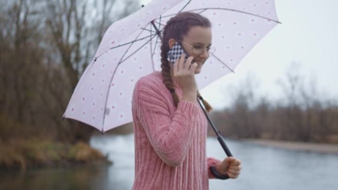 十几岁的女孩在雨天撑着伞，打电话