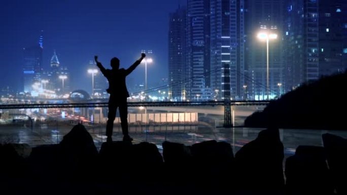 一名男子站在户外，举起手臂做胜利的姿势，展示成功的生活方式