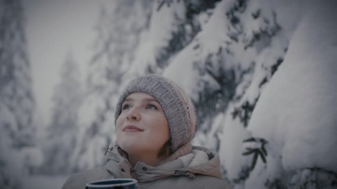 戴着手套的女人在白雪覆盖的森林里喝热饮料