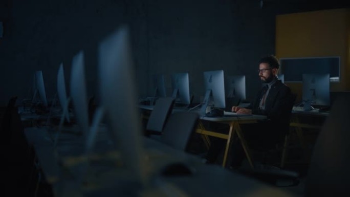 集中的男学生独自坐在大学信息学室，晚上在计算机科学项目上工作。年轻的学者在大学学习计算机，在课堂上编