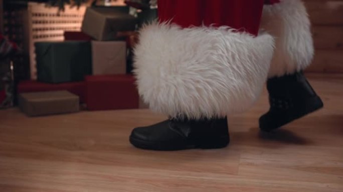 圣诞老人穿着靴子的脚的特写镜头，他走在装满礼物的房子的木地板上，我们看到他是如何来到树上，然后坐在椅