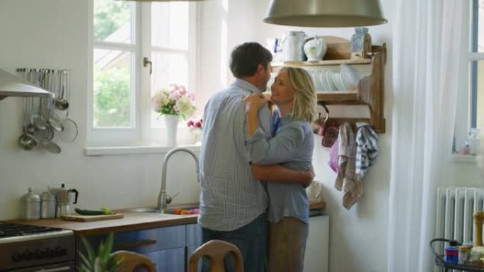 可爱的快乐成熟夫妇的真实照片是享受在一起的时光，并在家里的厨房里跳舞庆祝他们永恒的爱。
