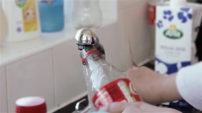女人的手在不锈钢厨房水龙头里用淡水装满一个空的可乐塑料瓶。特写。