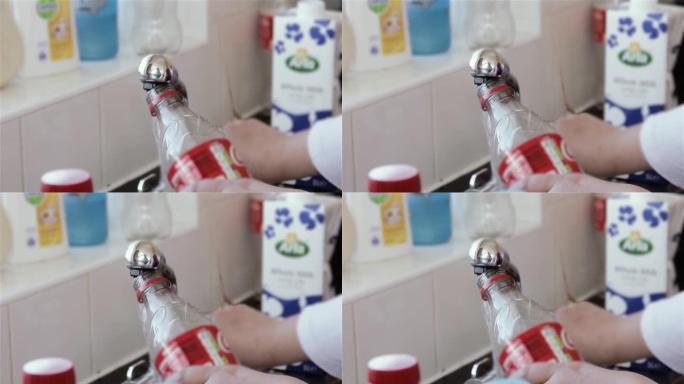 女人的手在不锈钢厨房水龙头里用淡水装满一个空的可乐塑料瓶。特写。