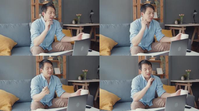 年轻的亚洲商人使用笔记本电脑与同事谈论视频通话计划，同时在客厅在家智能工作。