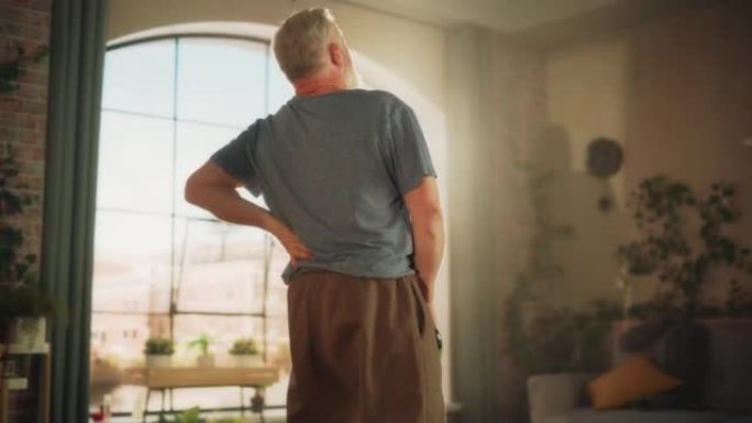 老年人在早上锻炼时会感到不舒服，突然背部疼痛，而在家用沉重的壶铃锻炼。中年男性抓住他的背来减轻疼痛。