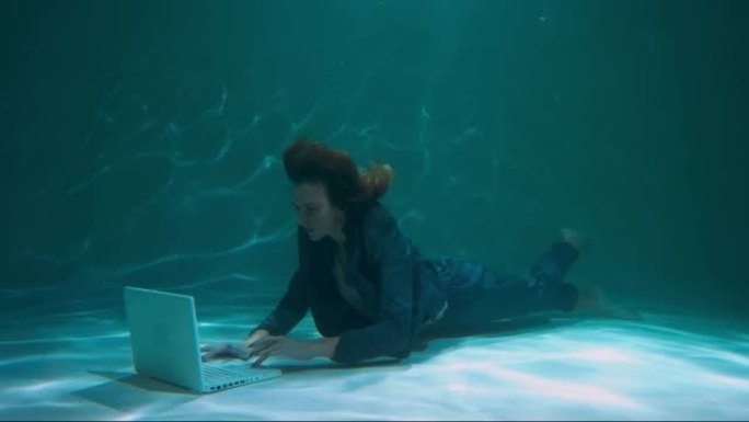 年轻美丽的工作狂老板女商人用笔记本电脑帮助客户慢动作的惊人水下镜头。