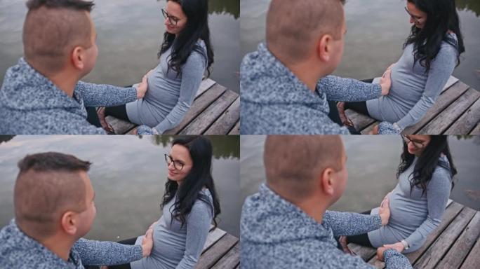 中年男子触摸坐在码头上的怀孕妻子的腹部