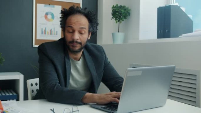 认真的阿拉伯雇员在办公室室内使用笔记本电脑打字