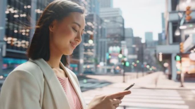 一位迷人的日本女性穿着时髦的休闲服行走并在城市街道上使用智能手机的肖像。大城市的经理与人们在线联系，