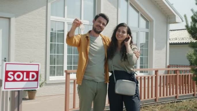 男人和女人的肖像新房子主人站在户外拿着钥匙拥抱微笑