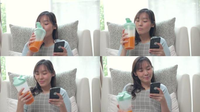 年轻女子在沙发上放松，在数字平板电脑上阅读并喝果汁